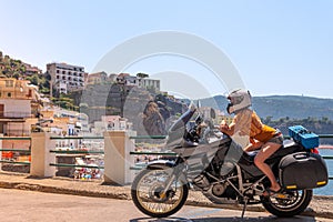Young girl posing. Motorcycle for tourism and travel. Wearing a helmet. In the background are views of the sea and hotels. Coast