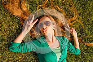 Young girl pouting and gesturing with two fingers while lying on grass