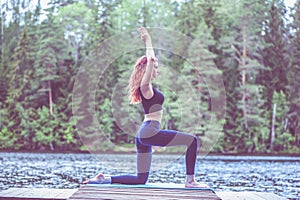 Young girl practicing yoga in the nature on the lake. Female happiness. Concept of healthy life and natural balance