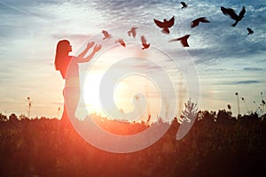 A young girl prays while enjoying nature amidst a beautiful sunset. The concept of hope, faith, religion. A flock of birds flies,