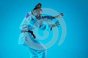 Young girl professional judoist isolated on blue studio background in neon light. Healthy lifestyle, sport concept.