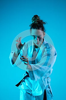 Young girl professional judoist isolated on blue studio background in neon light. Healthy lifestyle, sport concept.