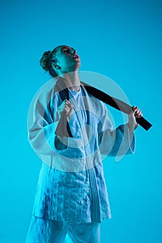 Young girl professional judoist isolated on blue studio background in neon light. Healthy lifestyle, sport concept.