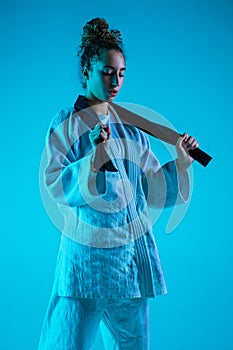 Young girl professional judoist isolated on blue studio background in neon light. Healthy lifestyle, sport concept.