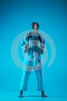 Young girl professional judoist isolated on blue studio background in neon light. Healthy lifestyle, sport concept.