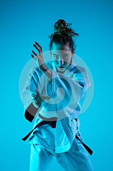 Young girl professional judoist isolated on blue studio background in neon light. Healthy lifestyle, sport concept.