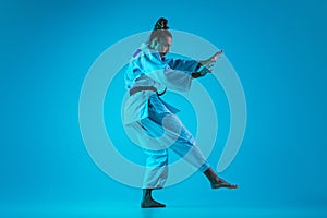 Young girl professional judoist isolated on blue studio background in neon light. Healthy lifestyle, sport concept.