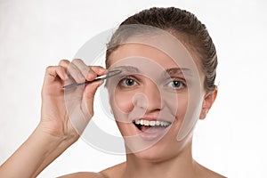 Young girl pulls out her eyebrows with tweezers metal on a white