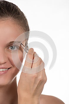 Young girl pulls out her eyebrows with tweezers metal on a white