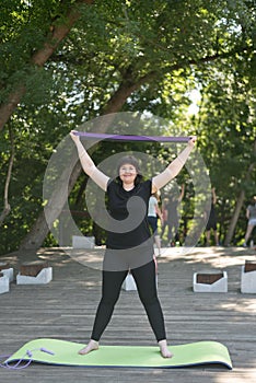 Young girl pump up arms with an expander. Fitness in the park. Vertical frame. Expander training for beginners. Individual