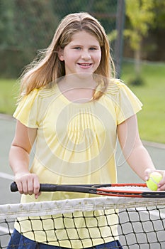 Young girl with racket on tennis court smiling