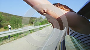 Young girl raise hands, scream out of open window of driving car. Wind. Smile. Traveling. Journey