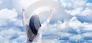 Young girl with raised arms. Against a background of blue sky and clouds. Joy. Prayer and worship to God.