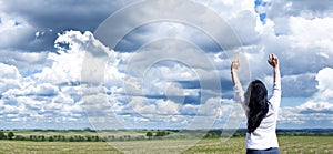 Young girl with raised arms. Against a background of blue sky and clouds. Joy. Prayer and worship to God.