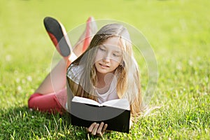 Young girl reading book lying on the grass