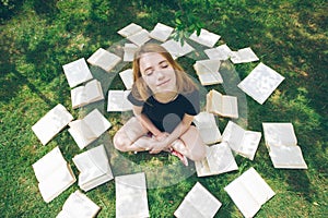 Young girl reading a book while lying in the grass. A girl among the books in the summer garden