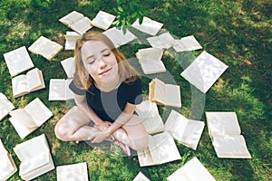 Young girl reading a book while lying in the grass. A girl among the books in the summer garden