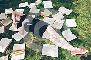 Young girl reading a book while lying in the grass. A girl among the books in the summer garden