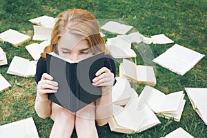 Young girl reading a book while lying in the grass. A girl among the books in the summer garden