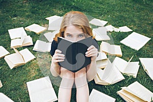 Young girl reading a book while lying in the grass. A girl among the books in the summer garden