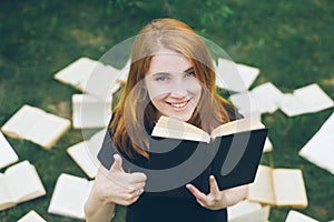 Young girl reading a book while lying in the grass. A girl among the books in the summer garden