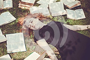 Young girl reading a book while lying in the grass. A girl among the books in the summer garden