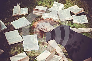 Young girl reading a book while lying in the grass. A girl among the books in the summer garden