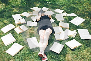 Young girl reading a book while lying in the grass. A girl among the books in the summer garden