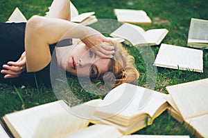 Young girl reading a book while lying in the grass. A girl among the books in the summer garden