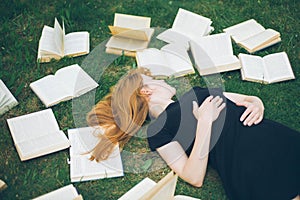 Young girl reading a book while lying in the grass. A girl among the books in the summer garden