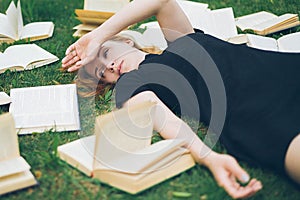 Young girl reading a book while lying in the grass. A girl among the books in the summer garden