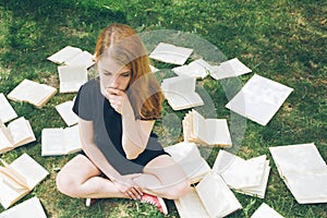 Young girl reading a book while lying in the grass. A girl among the books in the summer garden