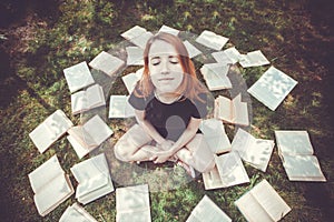 Young girl reading a book while lying in the grass. A girl among the books in the summer garden