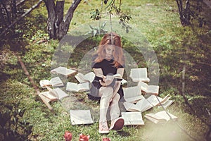 Young girl reading a book while lying in the grass. A girl among the books in the summer garden