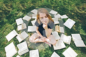 Young girl reading a book while lying in the grass. A girl among the books in the summer garden