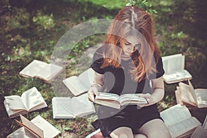 Young girl reading a book while lying in the grass. A girl among the books in the summer garden
