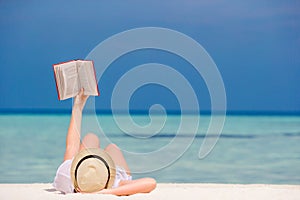 Young girl is reading a book lying on tropical white beach