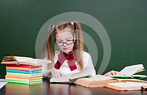 Young girl reading a book near empty green chalkboard