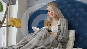 A young girl reading a book sitting in bed.