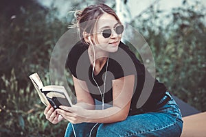 Young girl reading a book in the street.  female hipster enjoying literature outdoors. Smiling teen girl dressed in casual reading