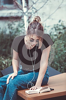 Young girl reading a book in the street.  female hipster enjoying literature outdoors. Smiling teen girl dressed in casual reading