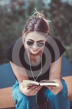 Young girl reading a book in the street.  female hipster enjoying literature outdoors. Smiling teen girl dressed in casual reading