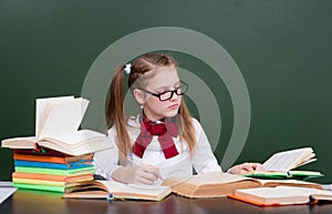 Young girl reading a books near empty green chalkboard