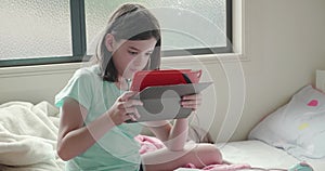 Young girl reading her tablet computer while home schooling in her bedroom during the coronavirus pandemic