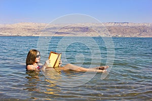 Young girl reads a book floating in the Dead Sea in Israel photo