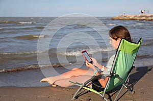 Young girl reads an ebook on the deckchair relaxing by the sea photo