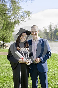 Young girl recently graduated, dressed in cap and gown, with her degree in her hands, celebrating with her father on the universit