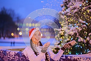 Young girl in a red cap stands near a Christmas tree. She throws