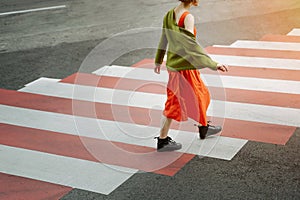 Young girl in red dress and green jacket crosses the road at a pedestrian crossing.