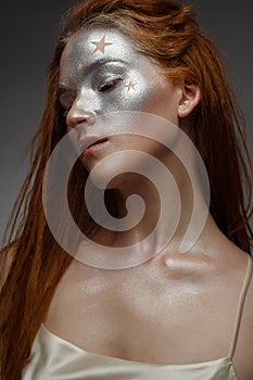 A young girl with red hair and a brilliant silver make-up with the stars. Beautiful model with shining skin. Holiday image.